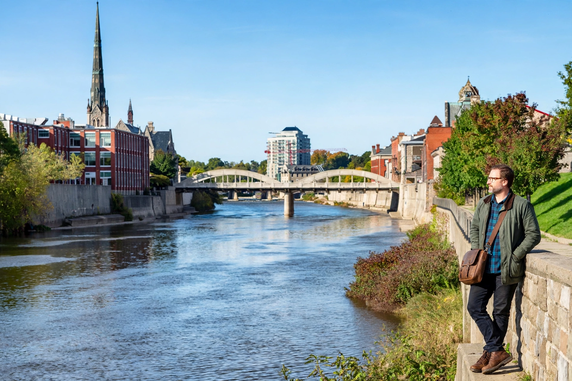 Cambridge business owner standing by the Grand River in downtown Galt, with the Main Street bridge and historic stone buildings behind her